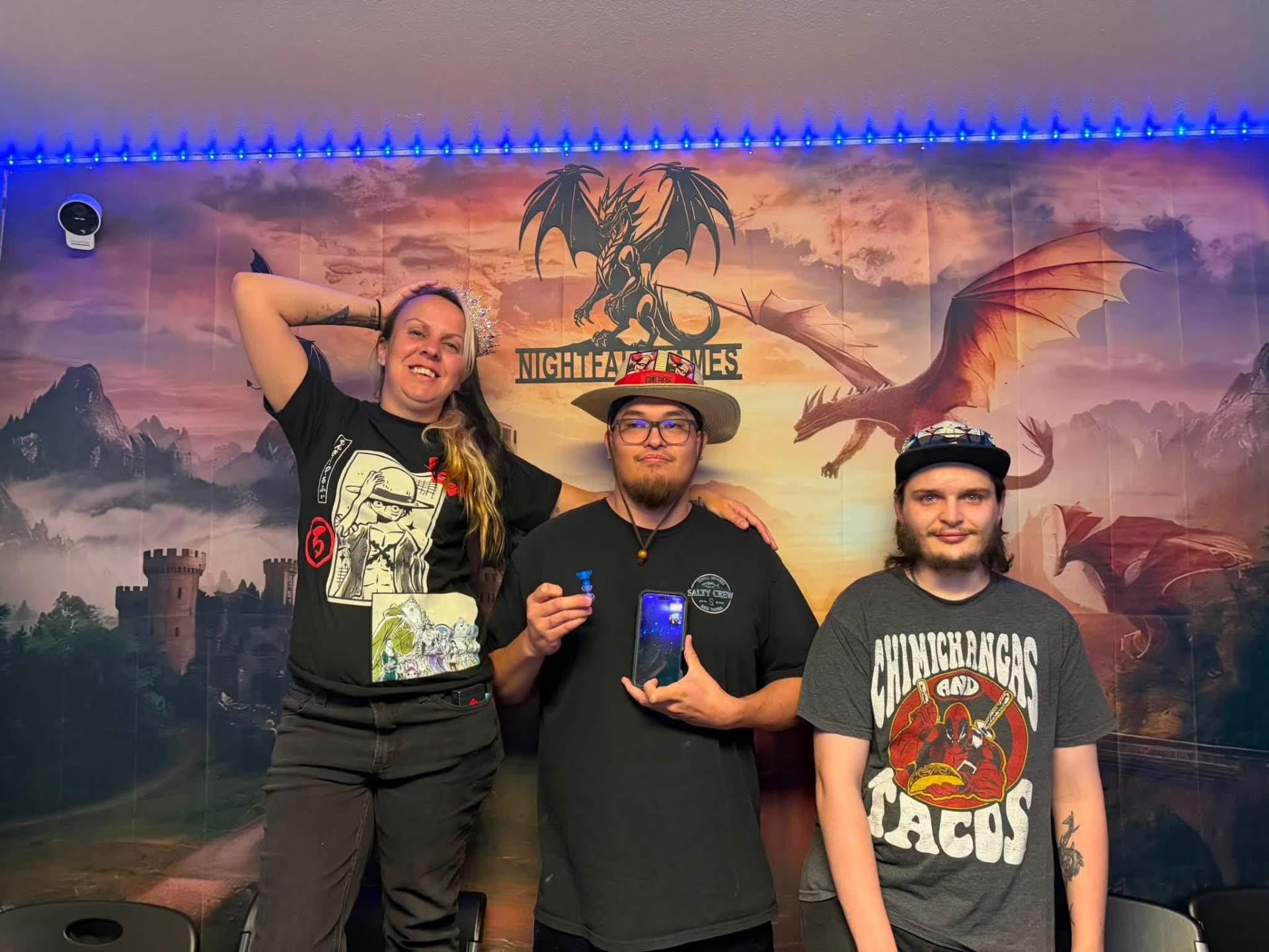 Top three finishers posing with a crown in front of the Nightfall Games™ dragon and castle backdrop after a One Piece Card Game event
