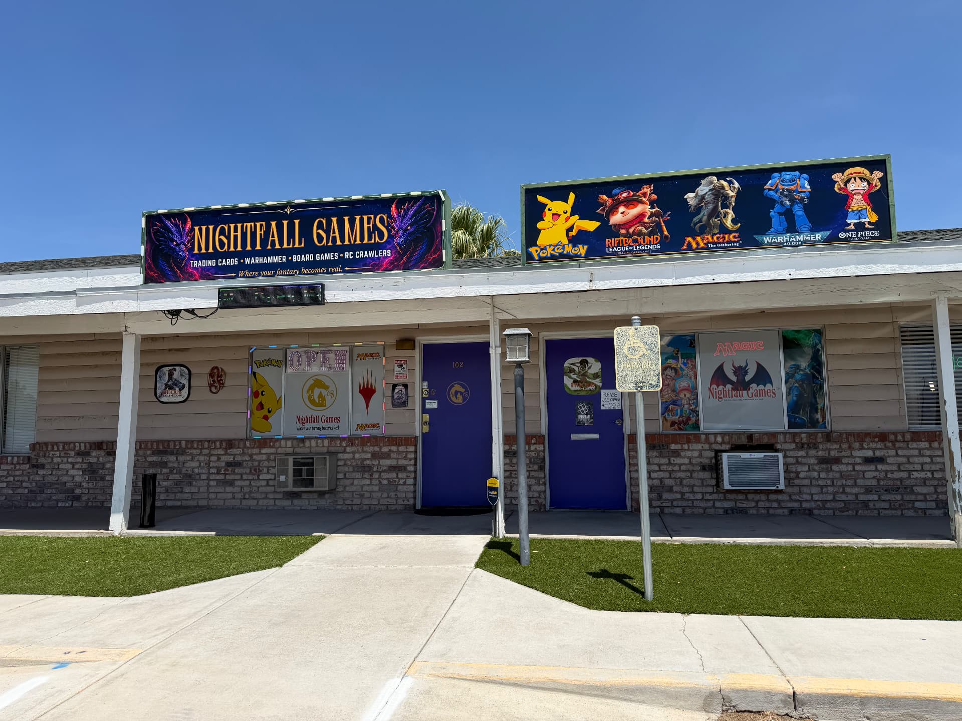 Full storefront of Nightfall Games™ in Pahrump, Nevada, with the dragon marquee sign reading Trading Cards, Warhammer, Board Games, RC Crawlers and a Pokémon, Riftbound, Magic, Warhammer and One Piece banner above the purple doors