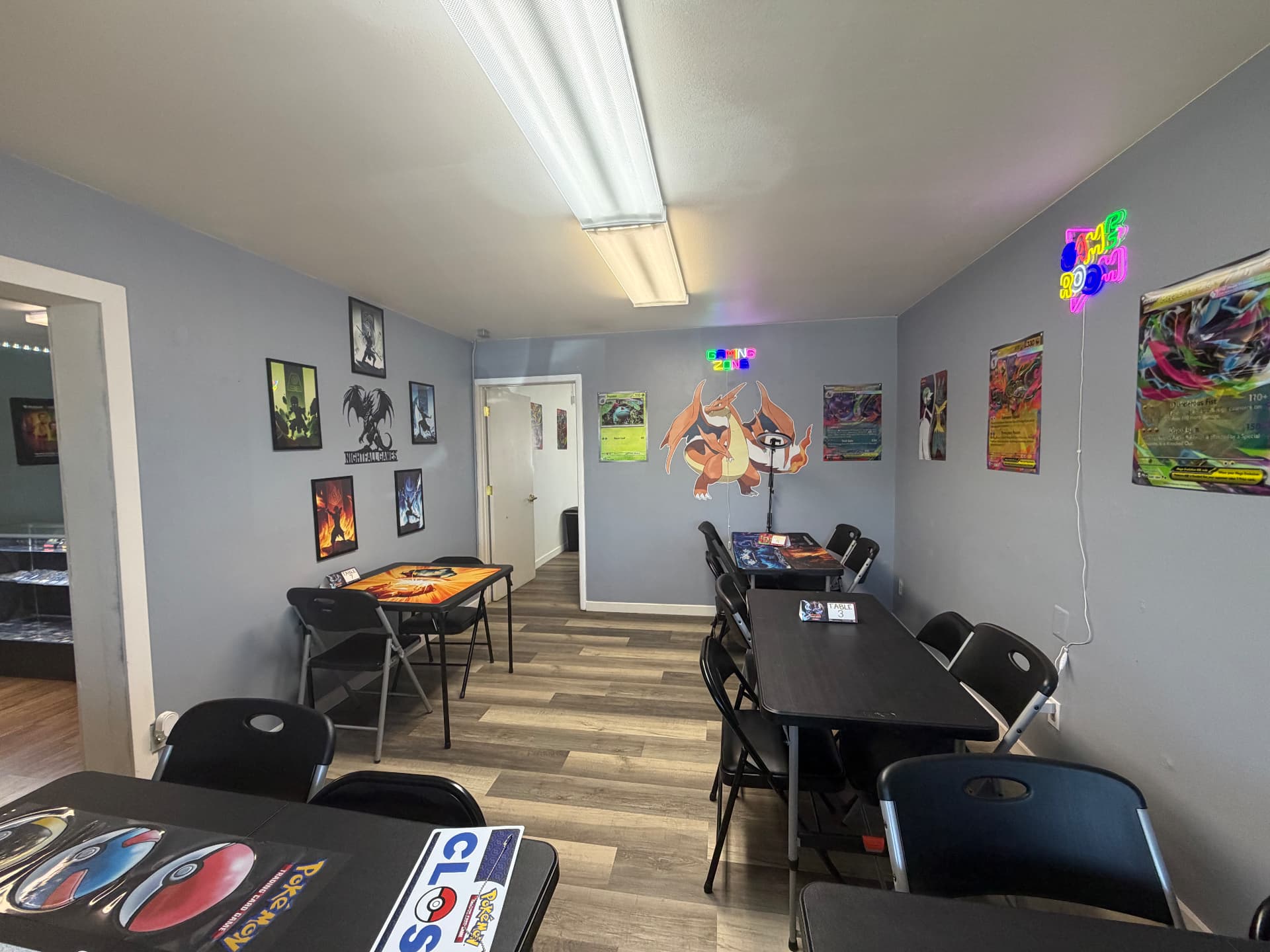 Wide view of the Nightfall Games™ game room showing numbered play tables, framed art and the Gaming Zone neon sign
