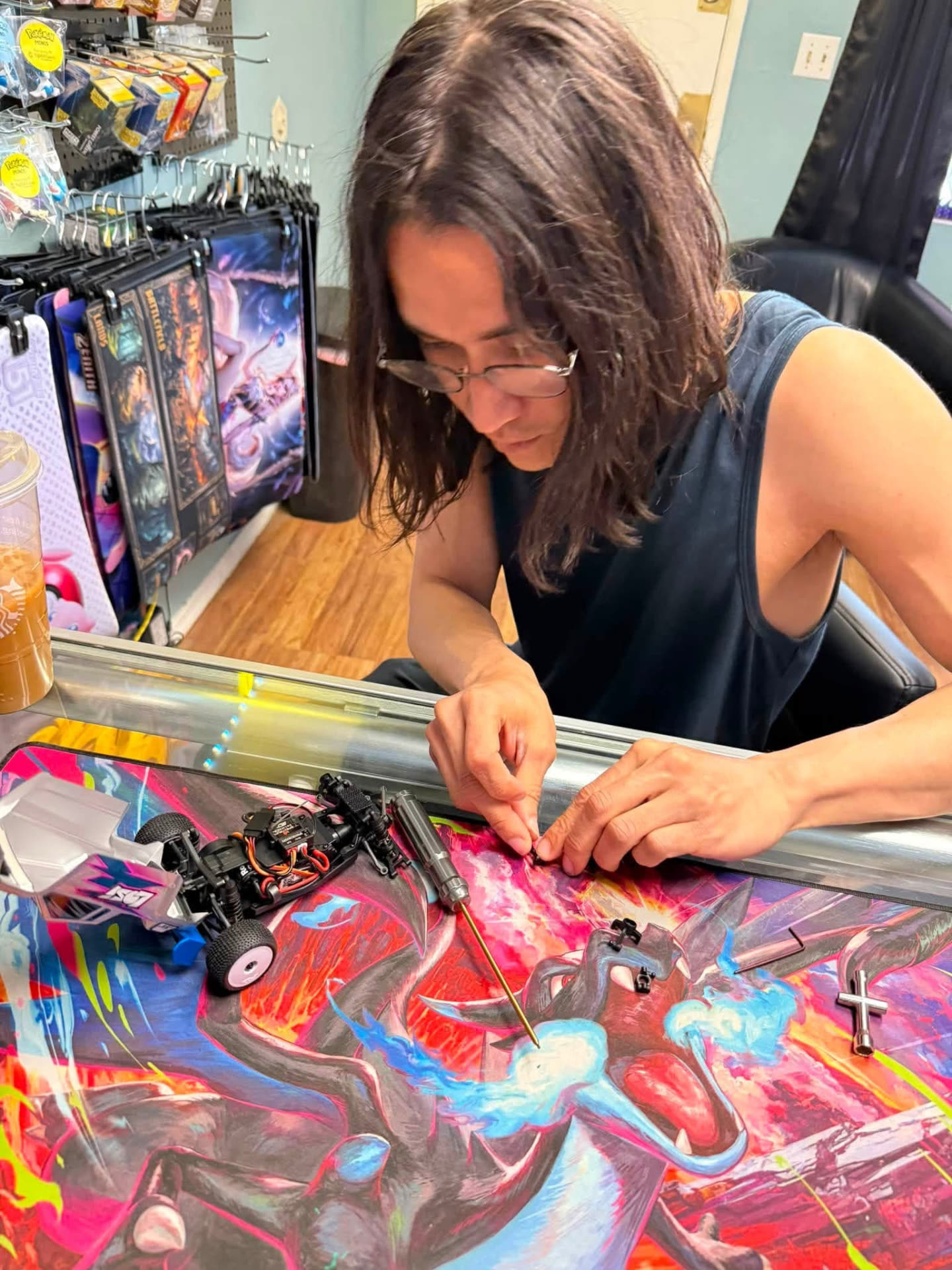 Hobbyist assembling an RC crawler chassis on a Charizard playmat at the Nightfall Games™ counter