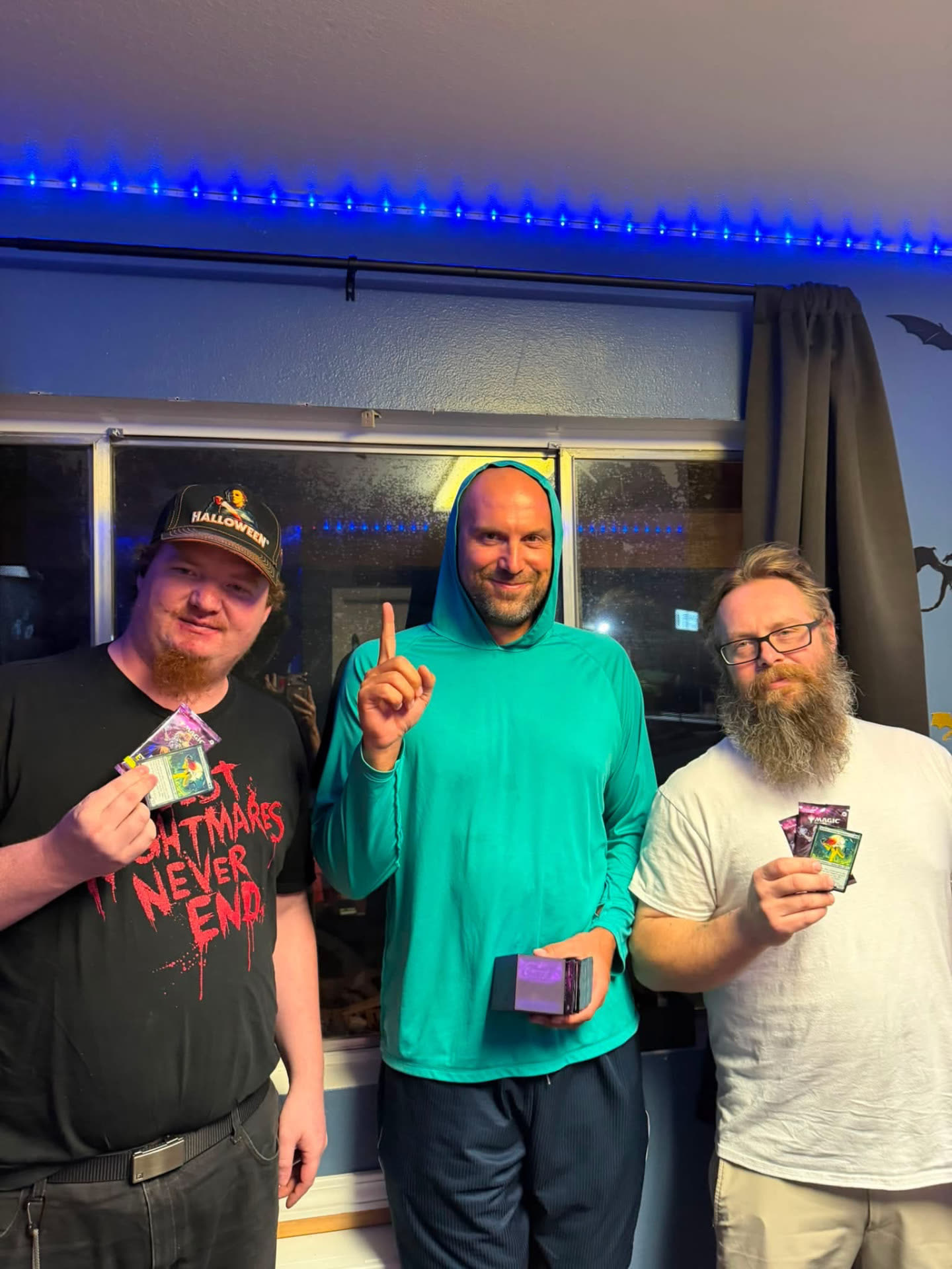 Three Magic: The Gathering players holding prize packs and a deck box after a Friday Night Magic event at Nightfall Games™